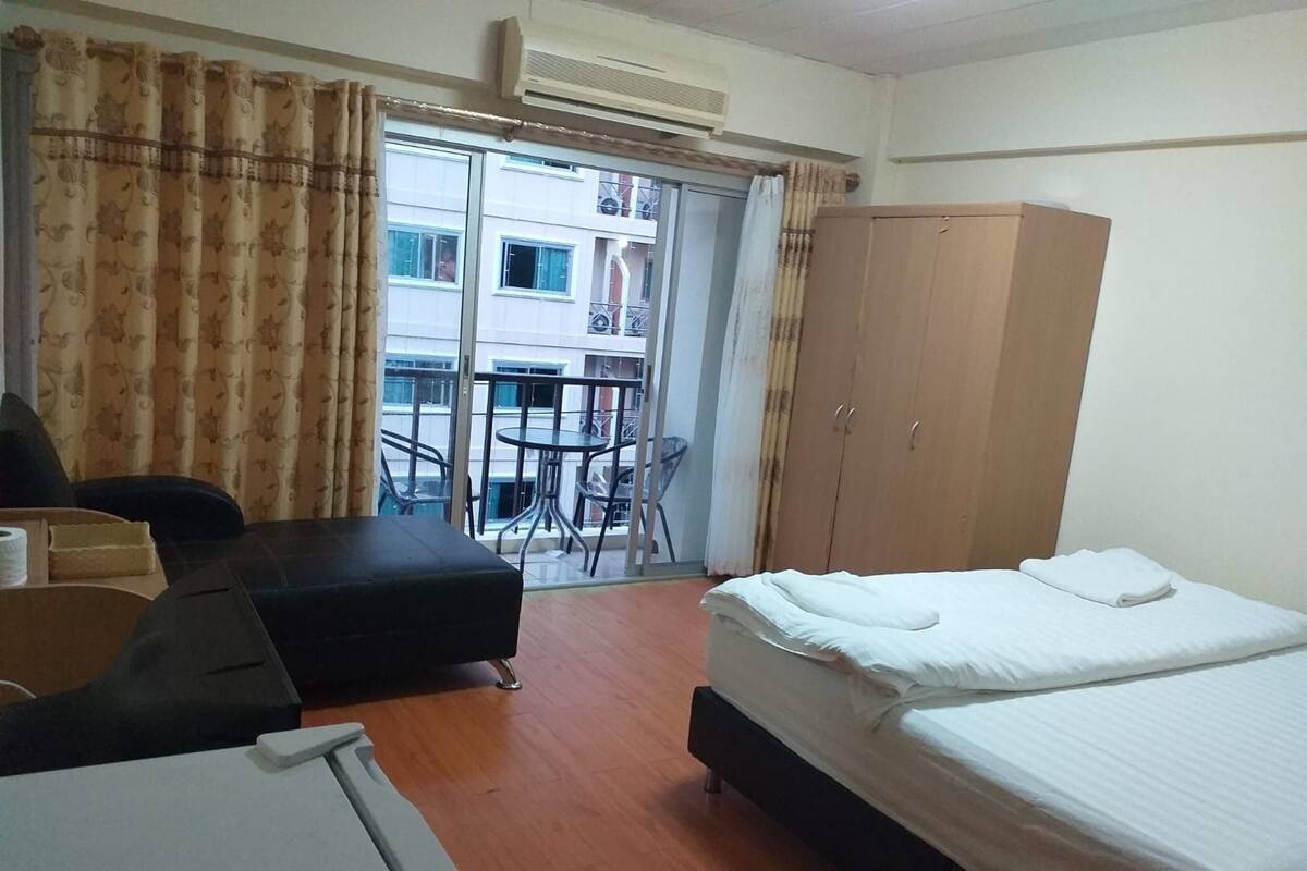 A hotel room with a bed, a desk, a chair, a wardrobe, and a balcony with a view of the building.
