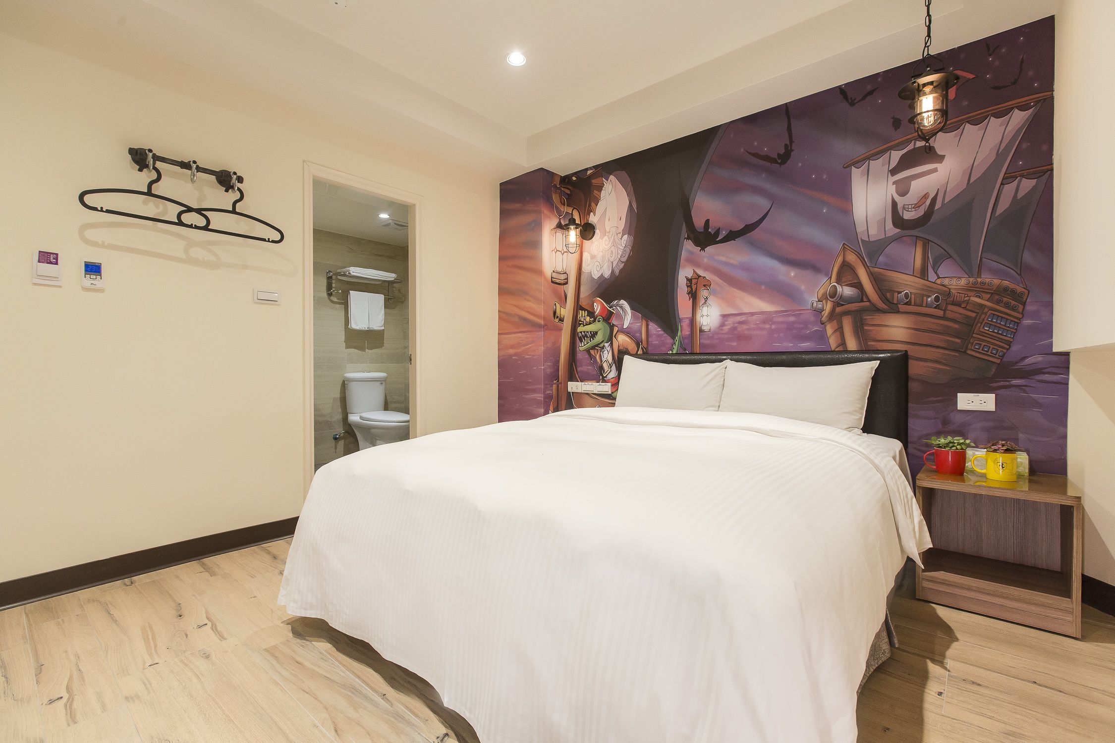 Quarto de hotel com cama, mesa de cabeceira, painel na parede e banheiro visível através de uma porta aberta.