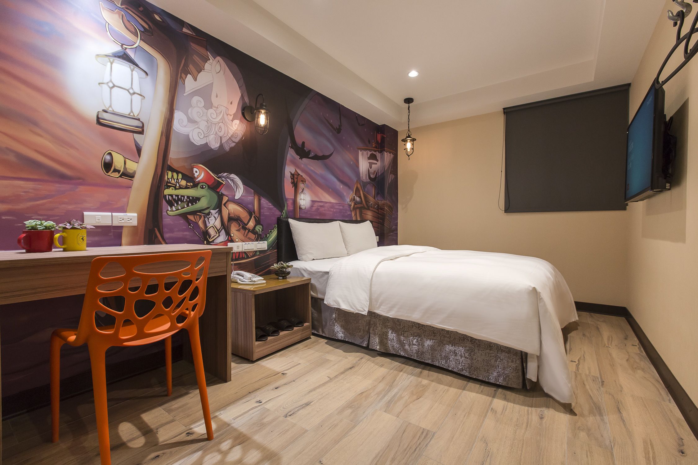Quarto com cama, escrivaninha com cadeira, TV na parede e um mural.