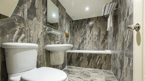 Une salle de bain moderne comprenant des toilettes, un lavabo et une zone de douche, avec des carreaux de marbre et une étagère intégrée.