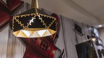 Una lámpara colgante de diseño geométrico con detalles negros y dorados, ubicada en una habitación con un mural de un teléfono rojo.