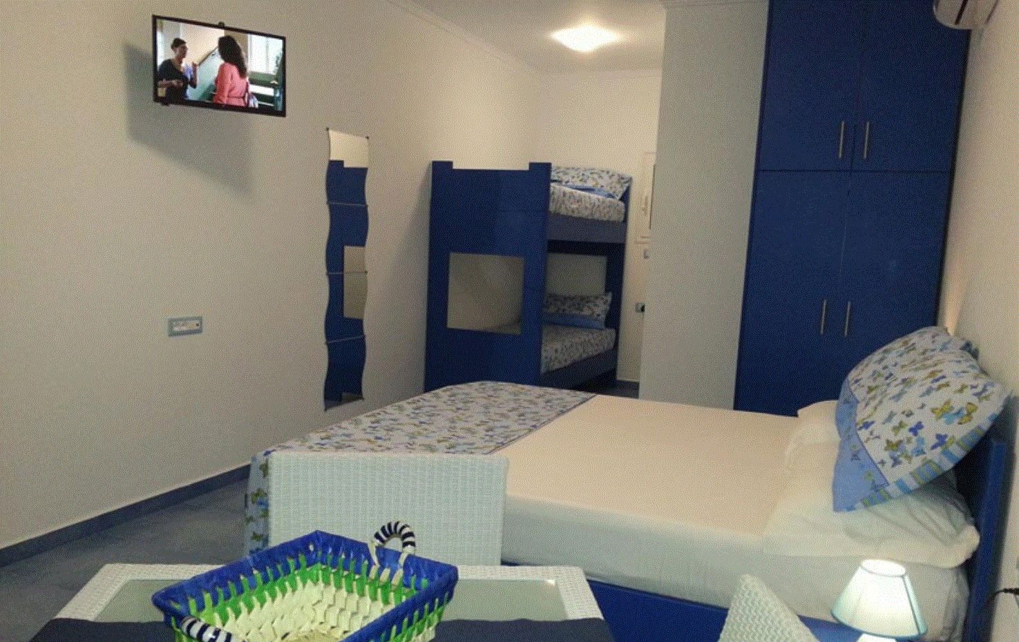 A bedroom with bunk beds, a television, a desk with a basket, and a lamp.