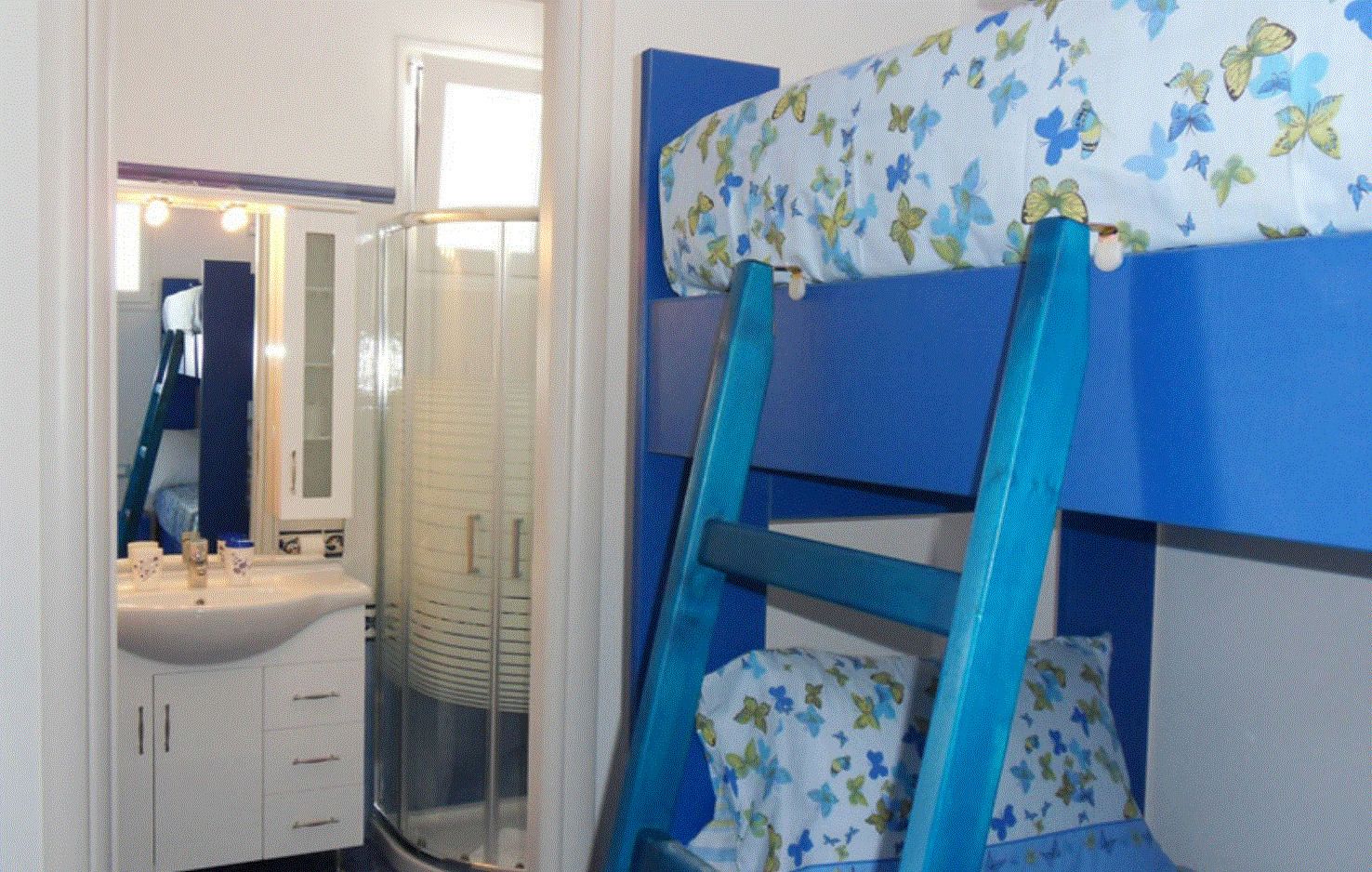 A bunk bed with a floral-patterned top bunk, a bathroom with a sink and mirror, and a glass shower enclosure.