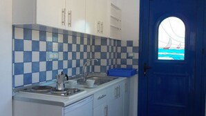 A kitchen with checkered blue and white tiles, a sink, and a stove. There is a blue door with a window showing a sailboat. - Bouganville Studios (Rhodes)