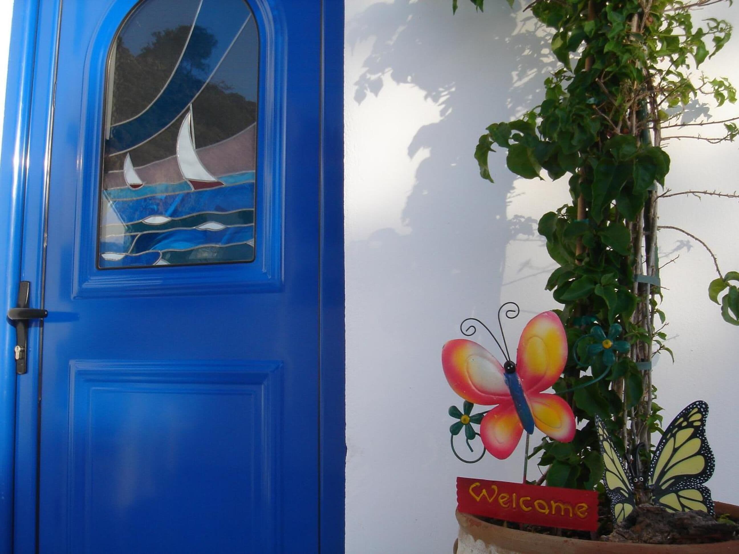 A blue door with a stained glass window and a welcome sign with a butterfly decoration.