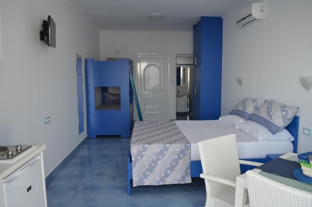 A compact hotel room with a bed, a small table, a chair, and a kitchenette.