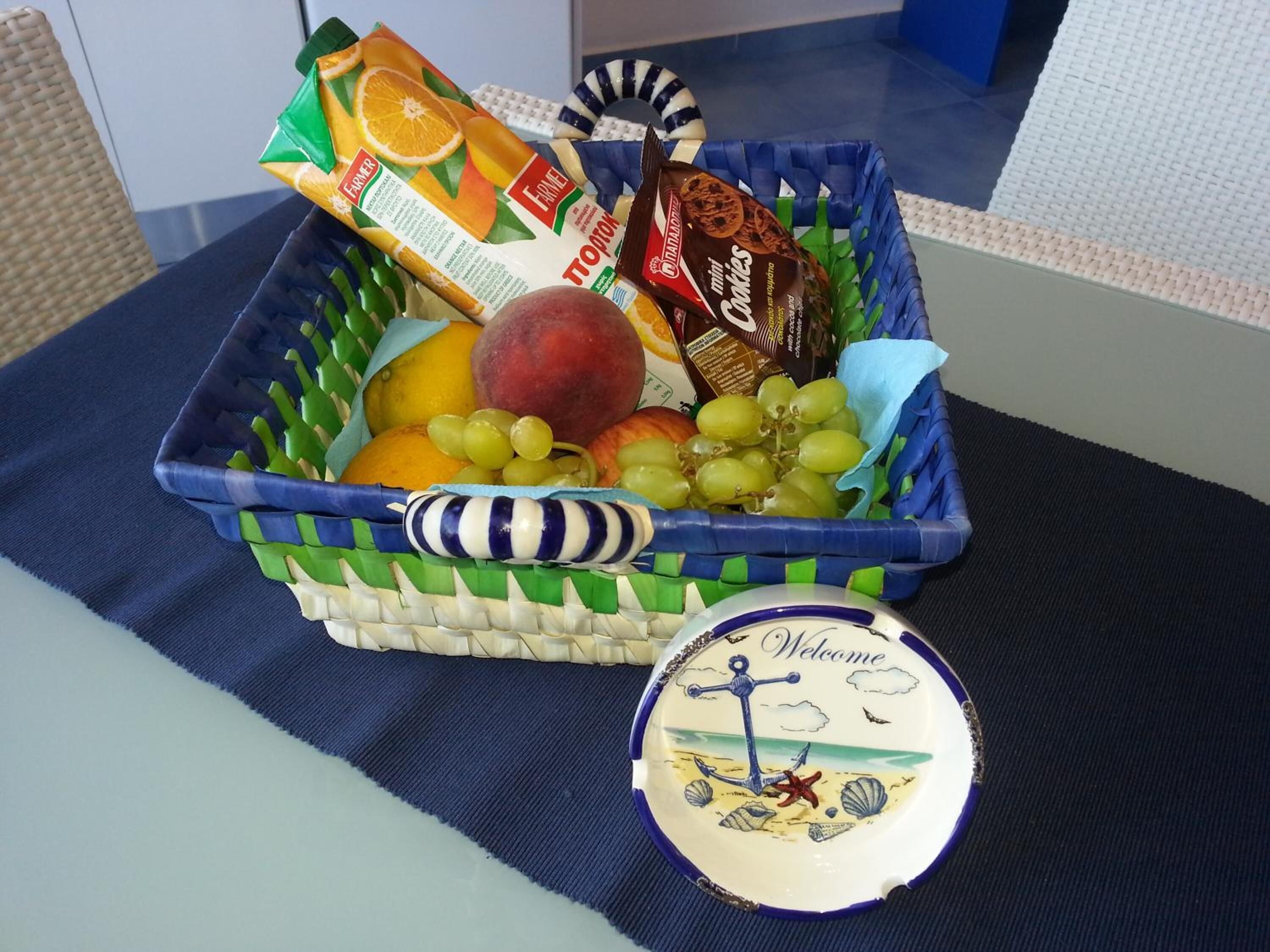 A fruit basket with a wicker basket containing oranges, grapes, and a peach, placed on a blue cloth.