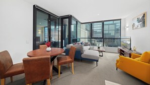 Un salon moderne comprenant un coin repas, un canapé, un fauteuil jaune et de grandes fenêtres.