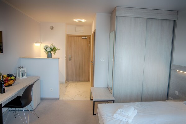 A modern hotel room with a bed, a desk with a chair, a small table, and a wardrobe.