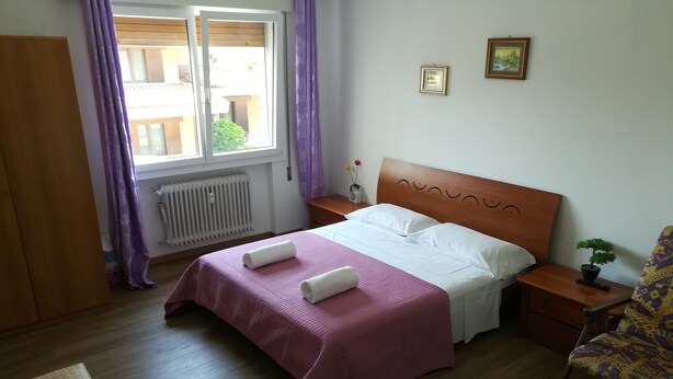A neatly arranged bedroom with a bed, a bedside table with a plant, a chair, and a wardrobe. - Venice Primavera Guesthouse  (Mestre)