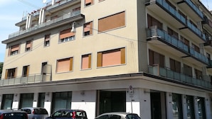 A multi-story building with balconies, a parking area, and a pedestrian crossing. - Venice Primavera Guesthouse  (Mestre)