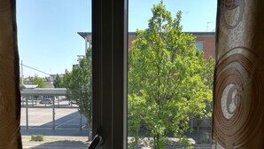 A view through a window with a metal railing, a parking lot, and a tree in the foreground. - Venice Primavera Guesthouse  (Mestre)