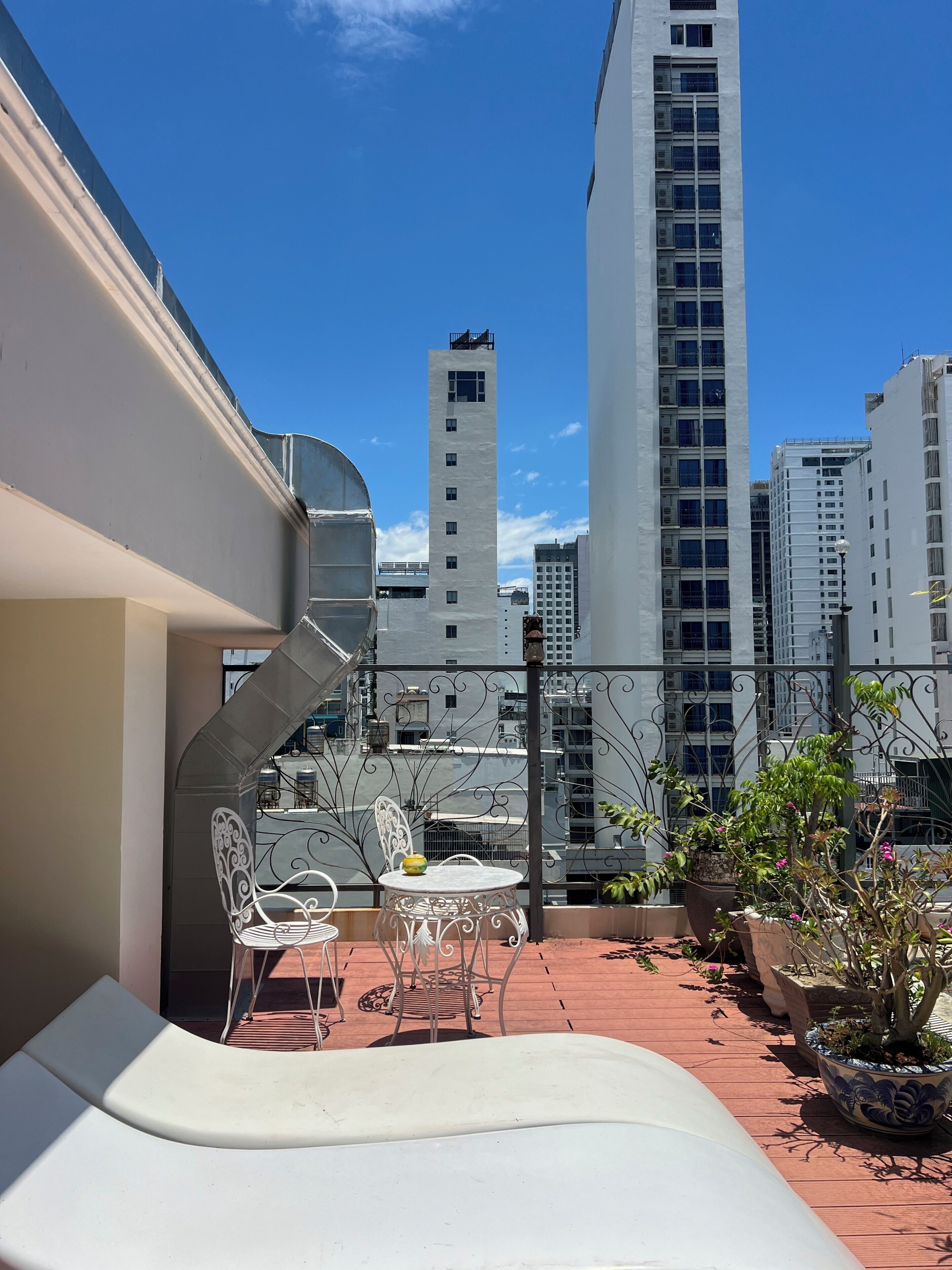 Une terrasse sur le toit avec une chaise blanche, une petite table et des plantes en pot.