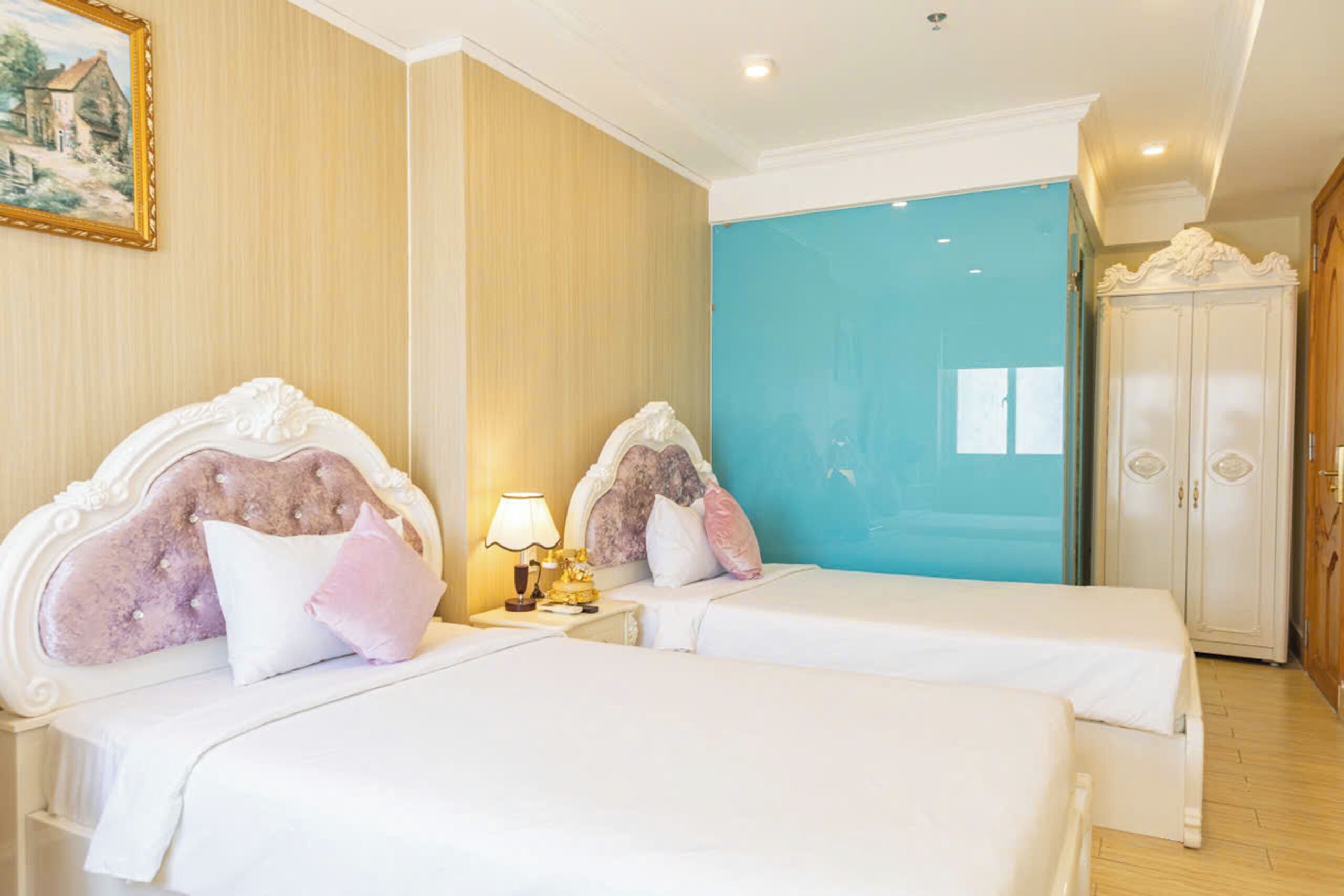 Een hotelkamer met twee bedden, een nachtkastje met een lamp, een kledingkast en een schilderij aan de muur.