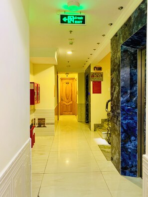 Un couloir d’hôtel avec une enseigne de sortie verte, une porte en bois portant le numéro 505 et un mur de marbre bleu.