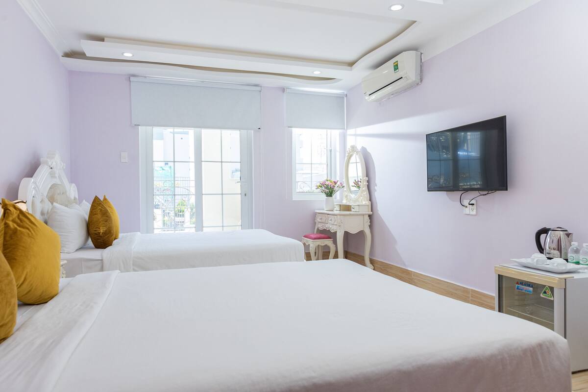 Ein Hotelzimmer mit zwei Betten, einem Fernseher, einem Schminktisch mit Spiegel und einer kleinen Küchenzeile.