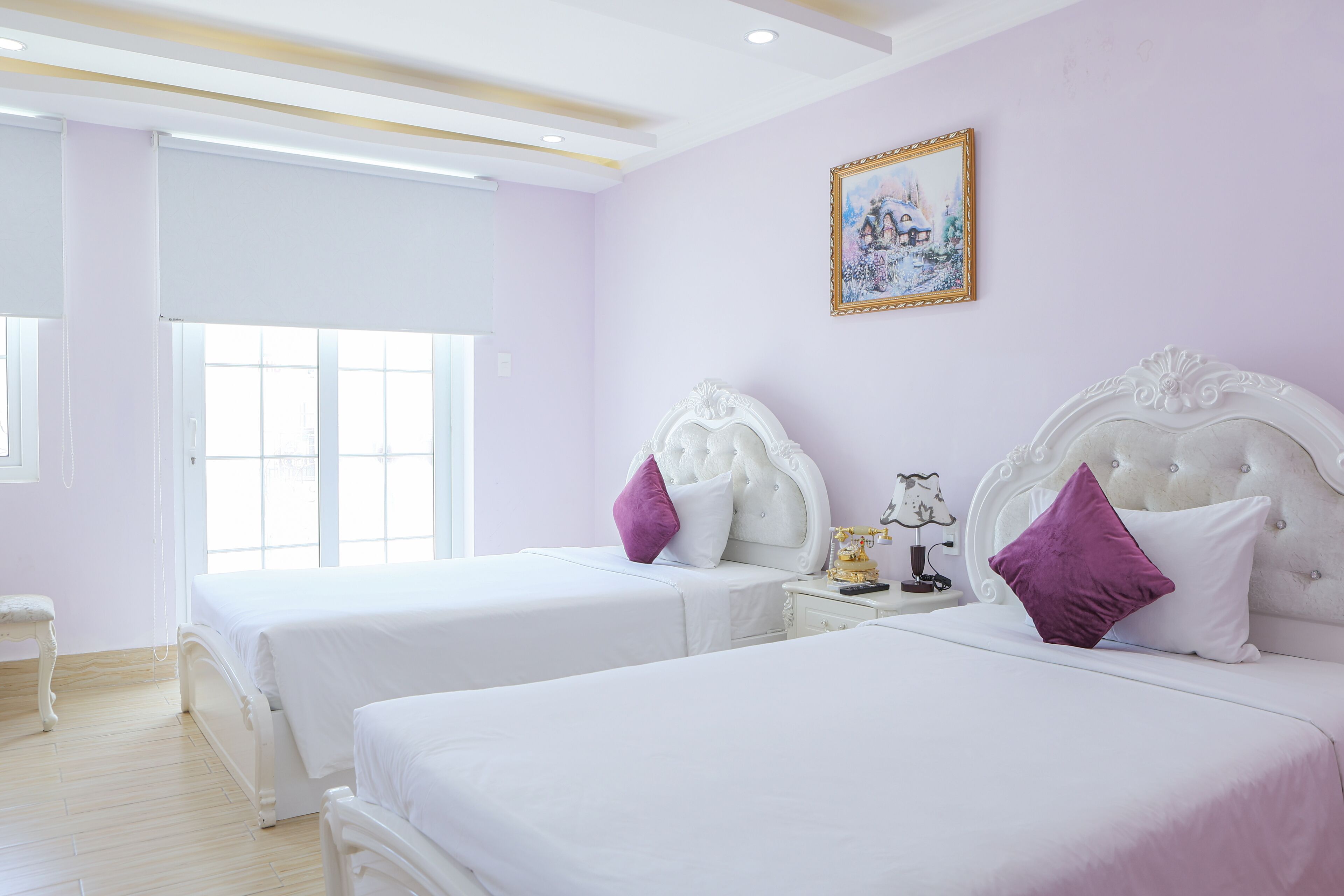 A room with two beds, a window, and a painting on the wall.