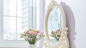Ein weißes Schminktischchen mit Spiegel, eine Vase mit rosa Blumen und ein roter gepolsterter Hocker.
