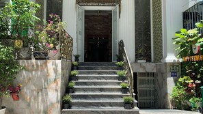 L’entrée d’un hôtel, avec des marches en marbre, une rampe en fer forgé et des plantes en pot.