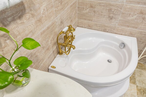 A bathroom with a white bathtub, a gold faucet, and a green plant in a glass vase.