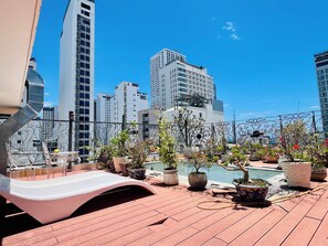 A rooftop terrace with potted plants, a pool, and a view of city buildings.