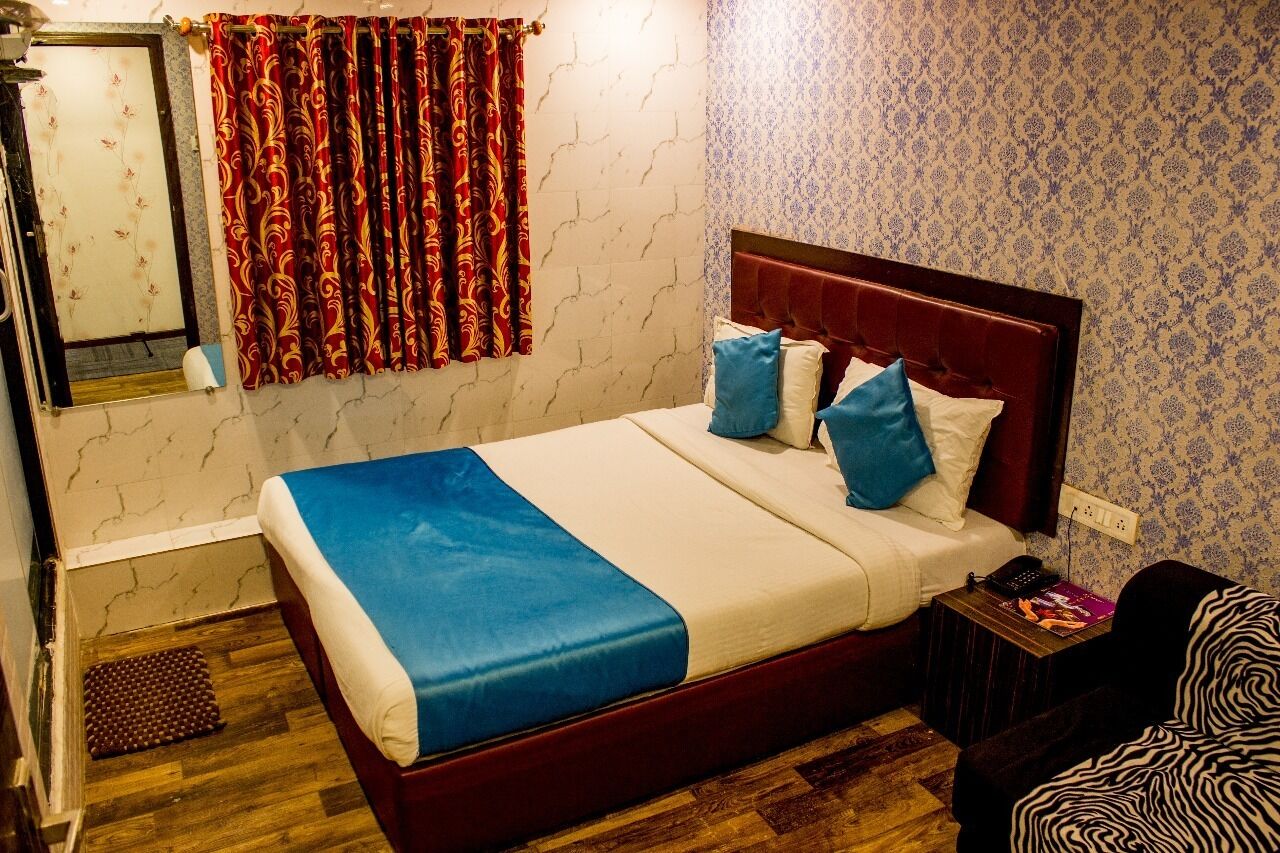A hotel room with a bed, a nightstand, a mirror, a window with curtains, and a patterned wall.