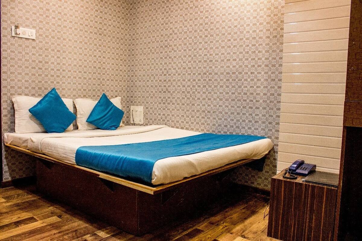 A neatly made bed with blue pillows and a blue bedspread in a room with patterned wallpaper and a wooden floor.