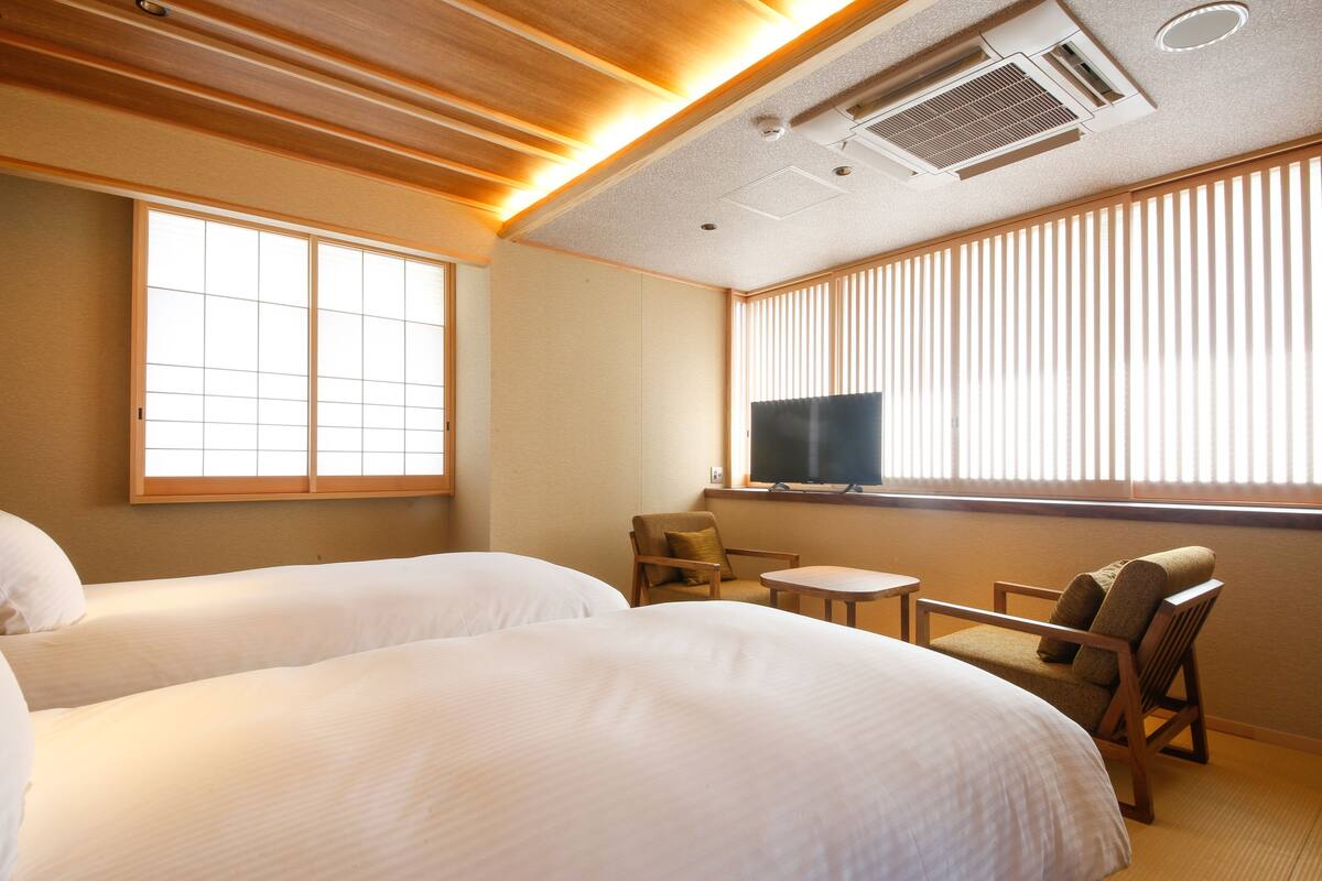 A hotel room with two beds, a television, a small table, and a chair.