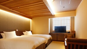 Habitación de hotel con techo de madera, dos camas con ropa blanca, un televisor sobre un mueble de madera y una pequeña silla de madera.