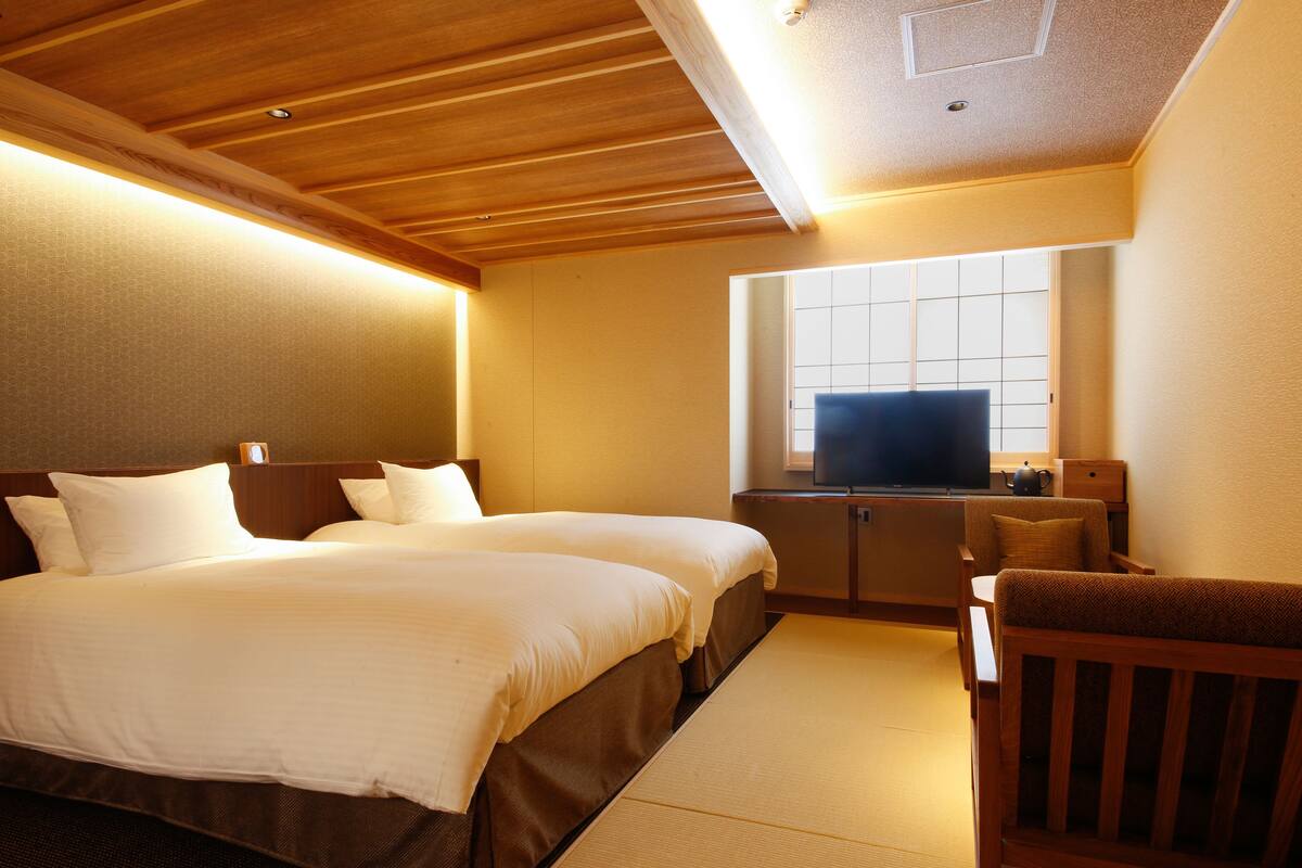 A hotel room with a wooden ceiling, two beds with white bedding, a television on a wooden cabinet, and a small wooden chair.