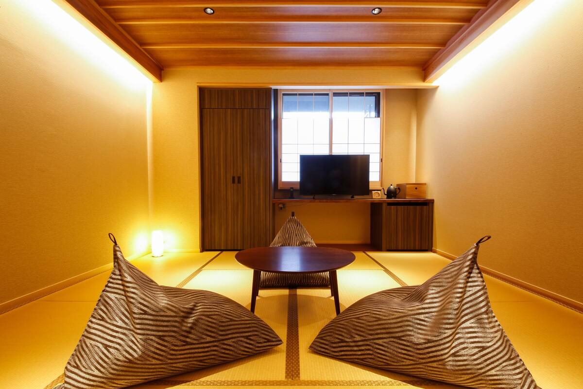 A traditional Japanese room with tatami flooring, a low table, two cushions, a television, and a sliding door.