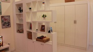A white storage unit with shelves and a cabinet, containing various items like baskets, framed photos, and decorative objects. - Suanson Paragon Green Villas (Rayong)