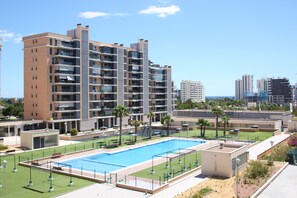 A modern hotel with a rooftop pool, multiple balconies, and a view of the city skyline. - Apt. CasaTuris Residencial San Juan (Alicante)