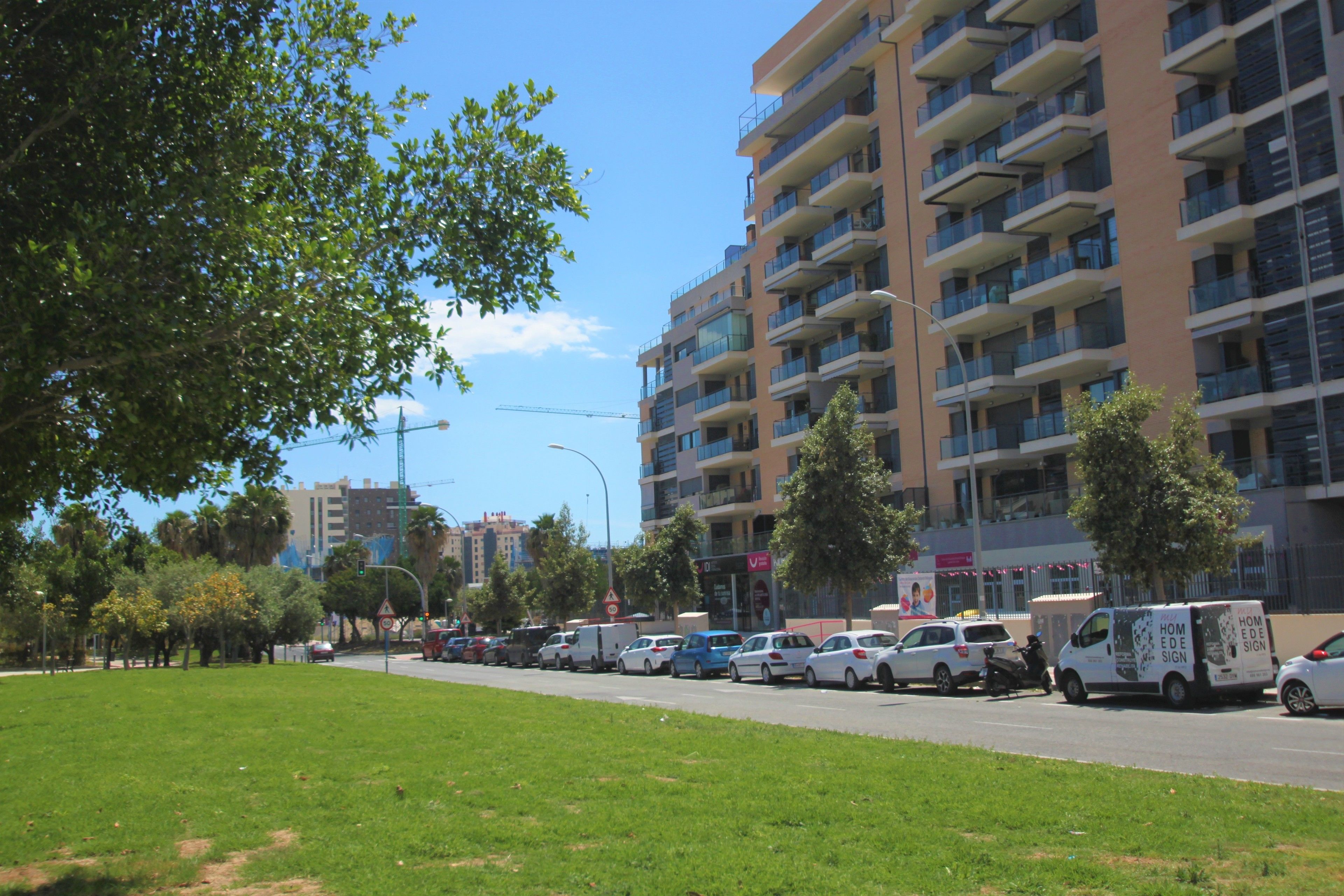 Un immeuble résidentiel à plusieurs étages doté de balcons, un parking avec des voitures et une zone herbeuse au premier plan.