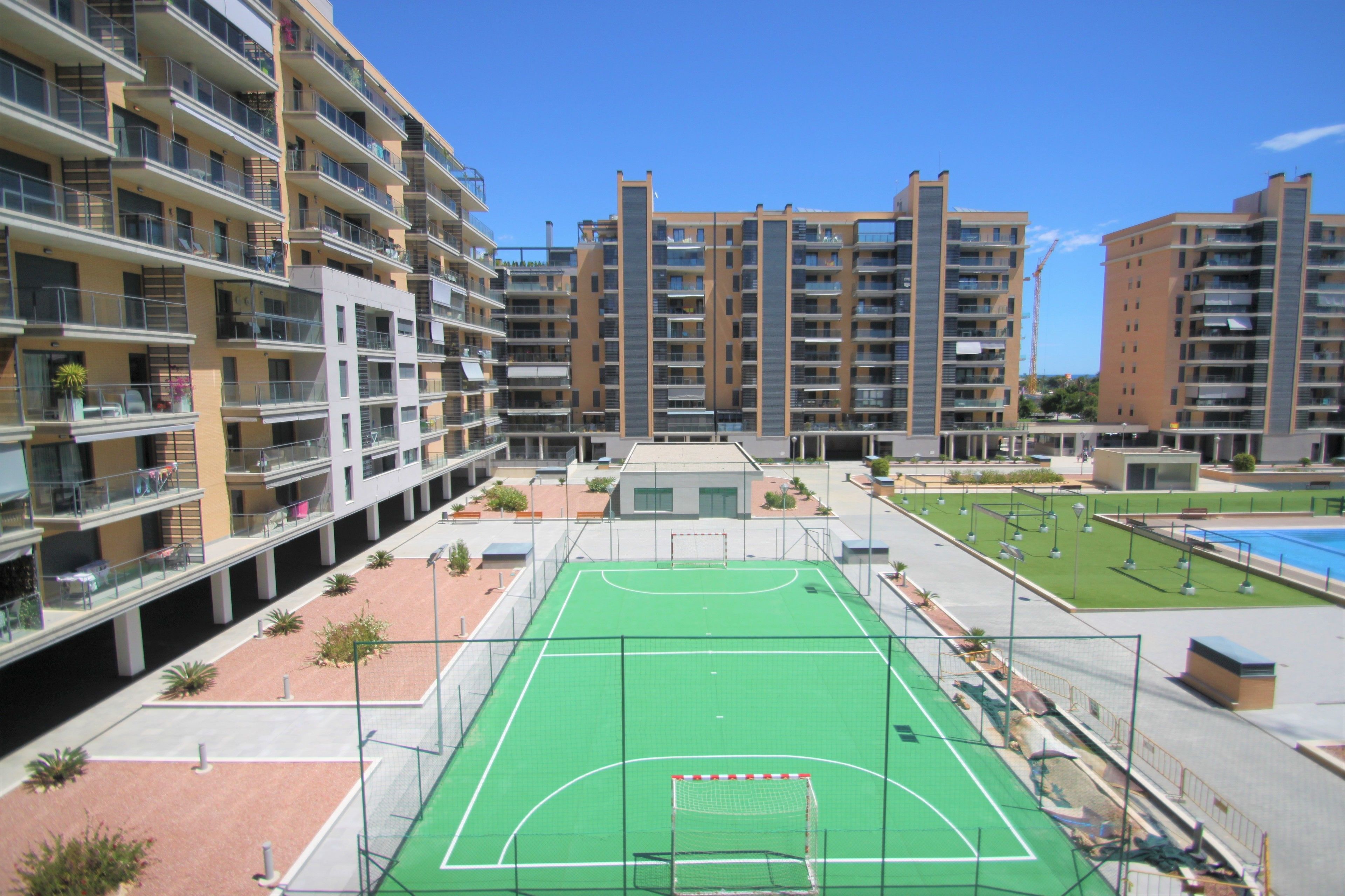 Een appartementencomplex met meerdere balkons, een groene sportveld en een helderblauwe lucht.