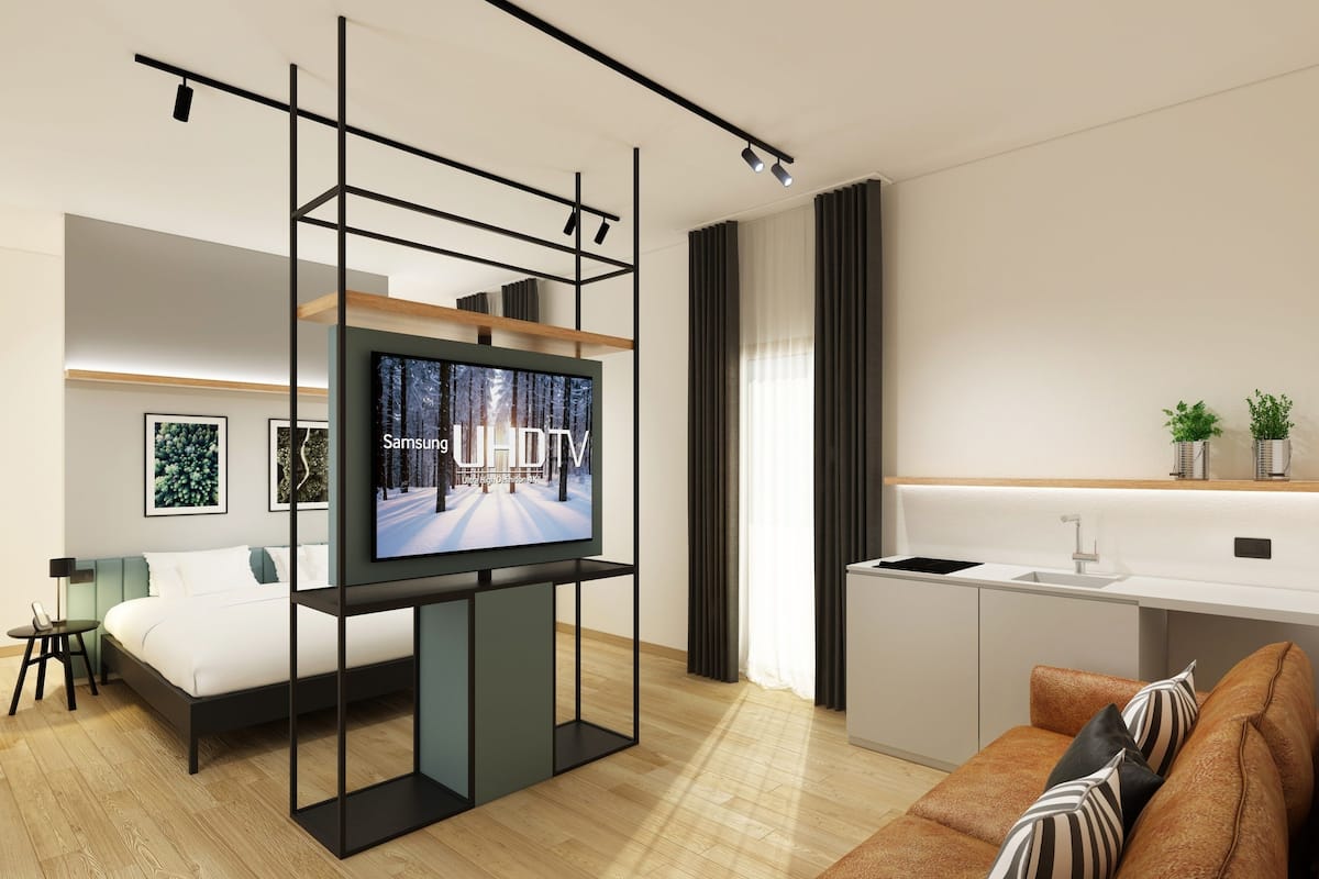 Una sala moderna con una televisión de pantalla plana montada en un marco negro, un sofá, una cama, una zona de cocina y una mesa de comedor.