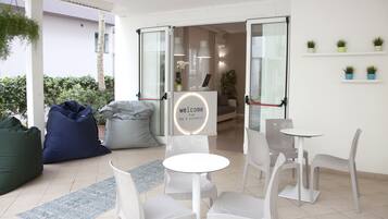 Een moderne binnenruimte met een receptie, witte stoelen, een kleine ronde tafel en een bord met de tekst welkom.