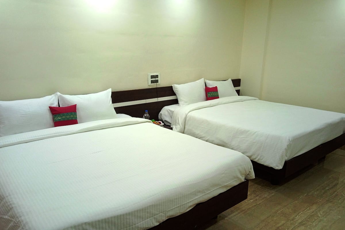 Two single beds with white linens and a headboard, a water bottle, and a power outlet on the wall.