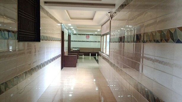 A hallway with tiled walls and a shiny floor, leading to a seating area with a bench and a table. - Sagar Resort (Chhatrapati Sambhajinagar)