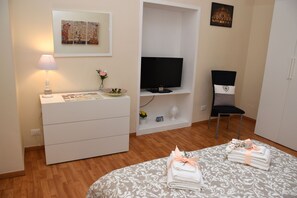 Habitación de hotel con cama, televisor, escritorio con lámpara, silla y armario.