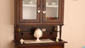 Un meuble en bois avec des portes en verre, un objet décoratif blanc posé sur le dessus et une horloge au mur.