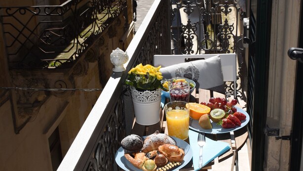 Un balcon avec une table préparée pour le petit-déjeuner, comprenant des fruits, des viennoiseries et un vase de fleurs.