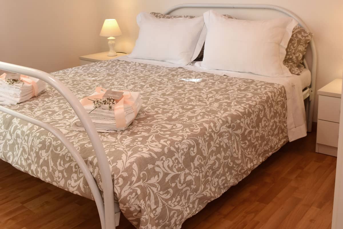 Un lit bien fait, recouvert d’une couvre-lit à motifs, une lampe de chevet et une décoration murale représentant des fleurs roses.