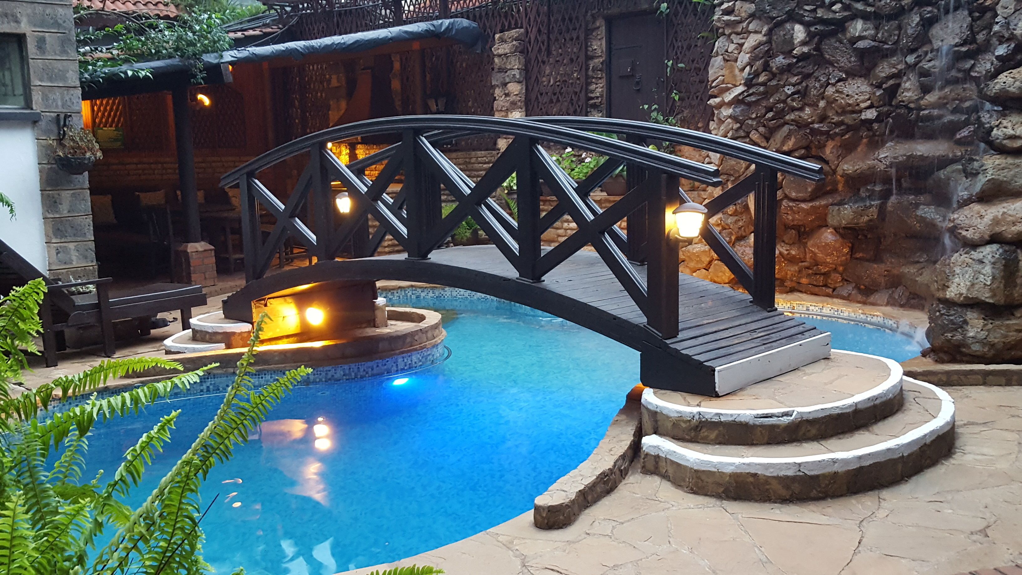 Ein Pool mit einer Steinbrücke, einer Feuerstelle und einer Steinmauer.