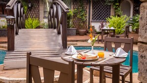 A dining table with a plate of food, a glass of orange juice, and a vase with flowers. - The Grand Gables (Nairobi)