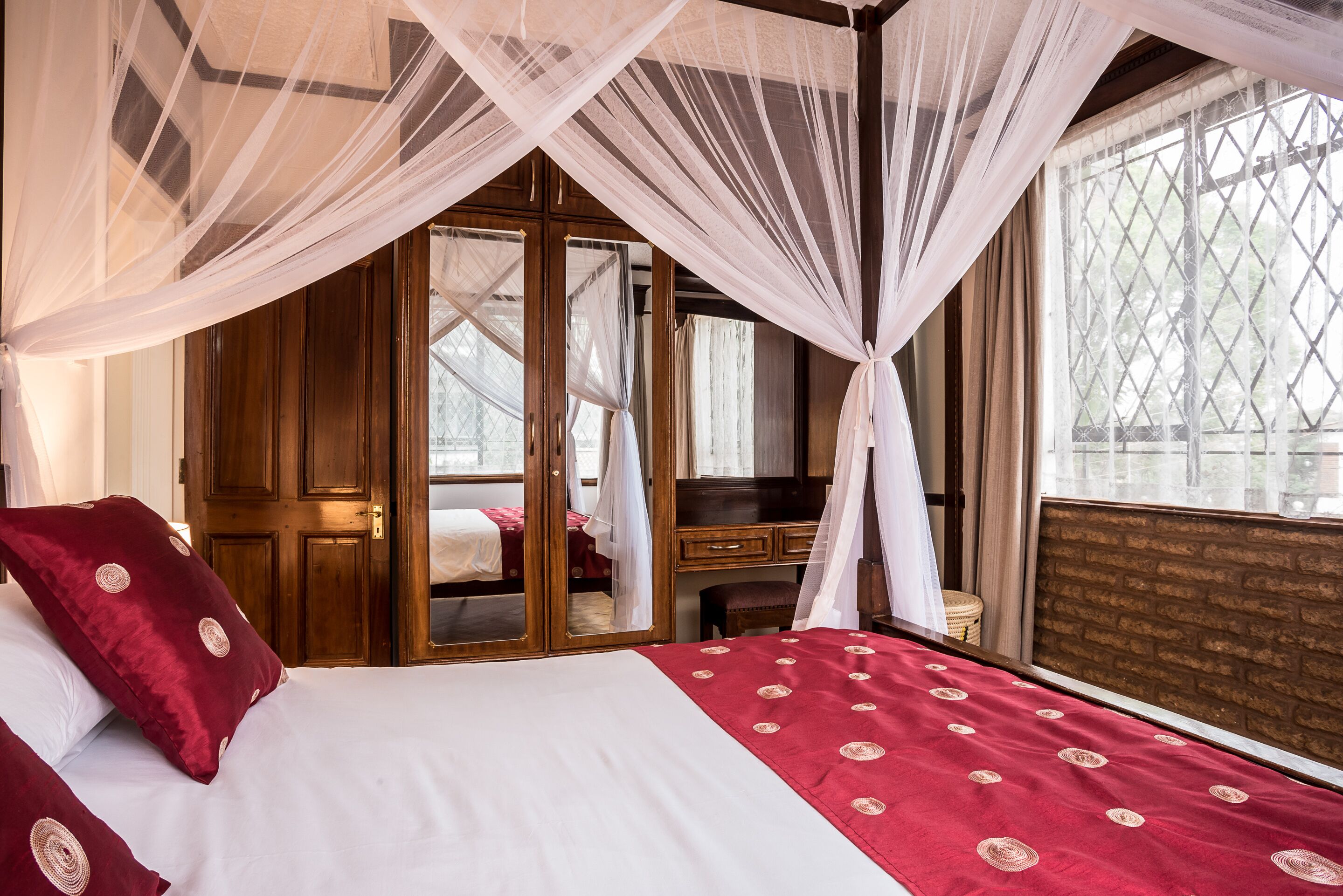 A bedroom with a bed, a wooden wardrobe, a desk, and a window with a view.
