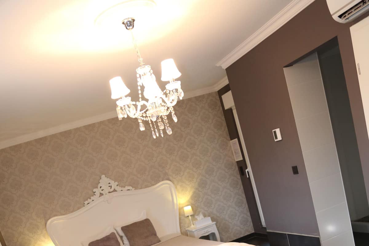Quarto com cama estofada branca, mesa de centro de vidro, candelabro e design moderno.