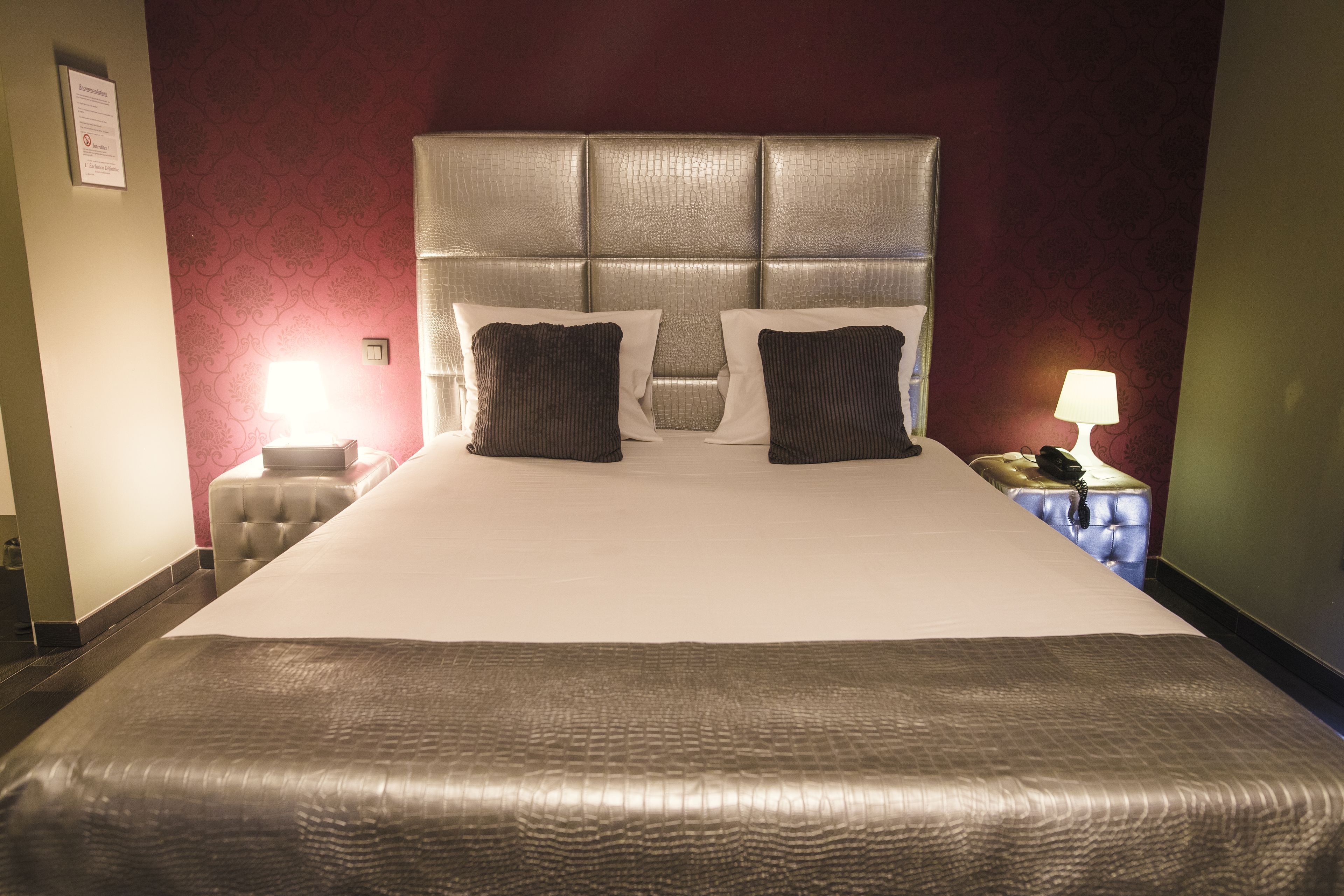 A hotel room with a large bed, two bedside tables, a lamp, and a red patterned wall.