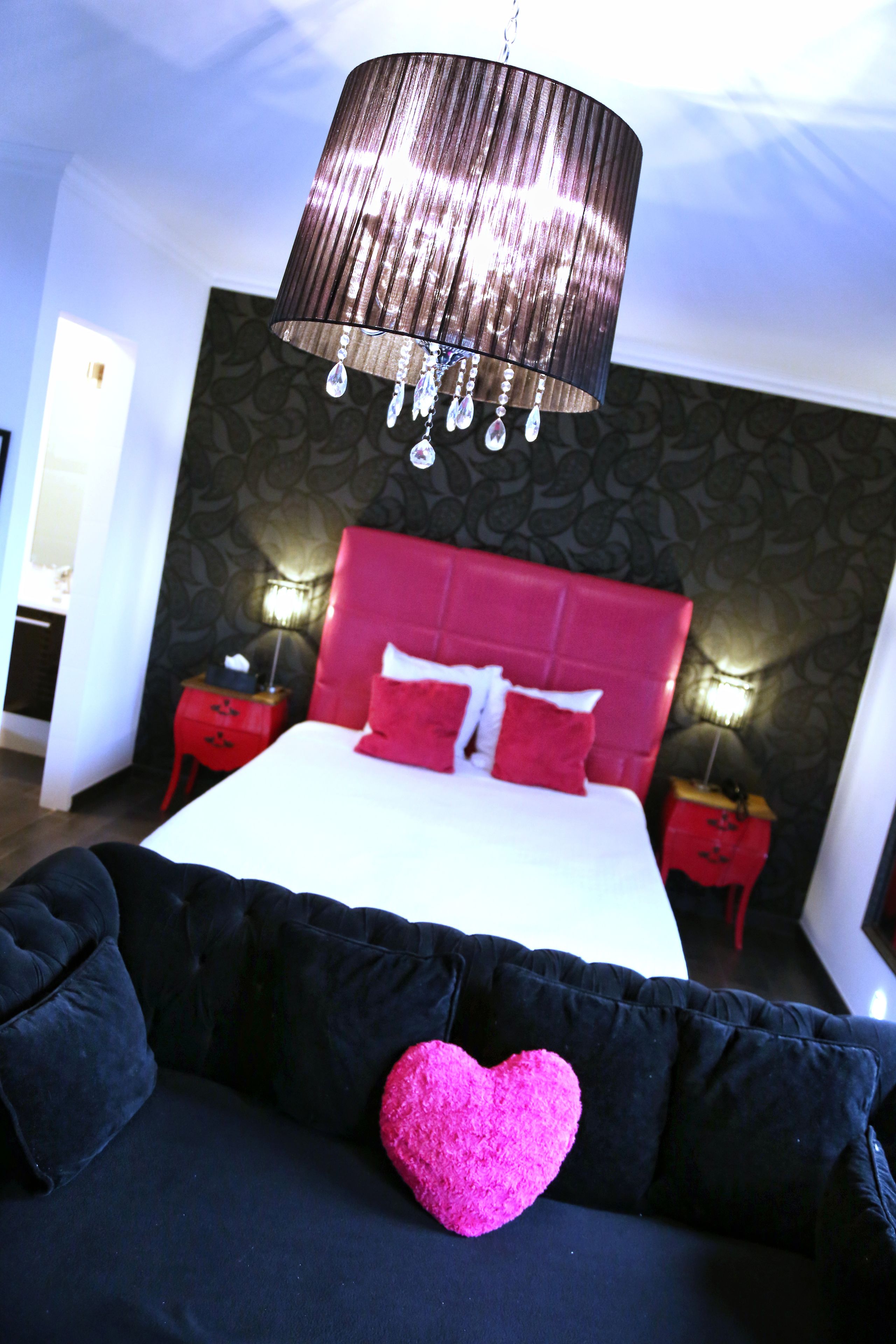 A modern bedroom with a large bed, red headboard, and black and pink pillows.