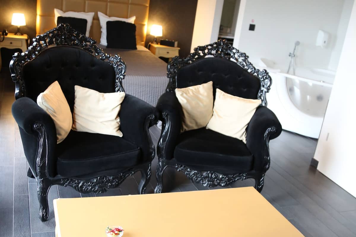 Quarto moderno com uma cama, duas cadeiras pretas e elaboradas, uma mesa pequena e um candelabro.